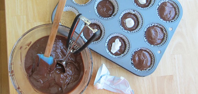 Beat cupcake mix, water, oil and eggs on low speed for 30 seconds then on medium speed for two minutes. Pour enough batter into each cupcake cup to cover the crust. 
Knead the marshmallow packet and snip off one tip. Squeeze some marshmallow into the center of each of the cupcakes. Pour the