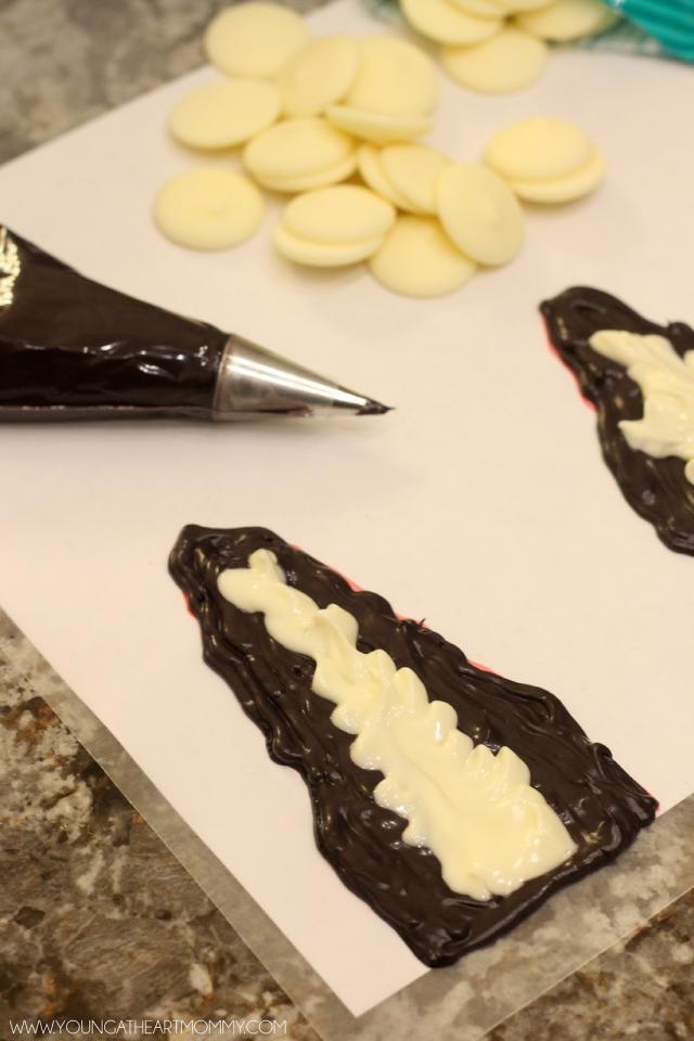 For the Bride of Frankenstein you will need to pipe her signature hair piece out of chocolate candy melts. Using a piece of white paper, free-hand her hair with a pencil or marker. Remember to add an area in the shape of a lightening bolt in the middle.