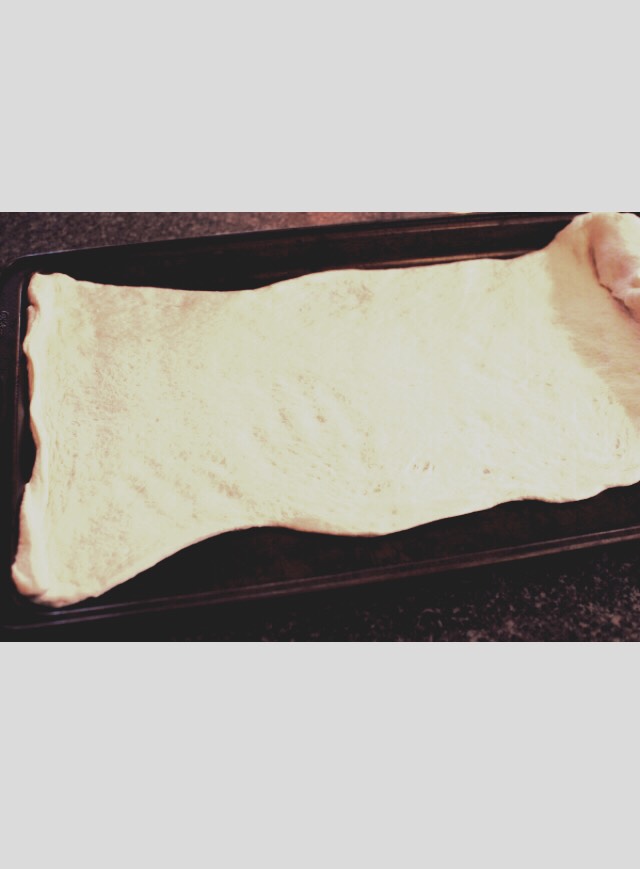 You start by rolling out a store-bought pizza dough. Get it as long and flat as you can. It doesn’t have to be perfect.