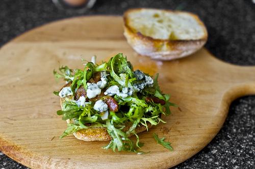 Remove rolls from toaster and divide bacon-frisee salad between each bottom bun. You’ll want to heap on more than seems feasible or needed, especially once you realize how tasty it is. Top each salad pile with half (2 tablespoons) of the blue cheese. 