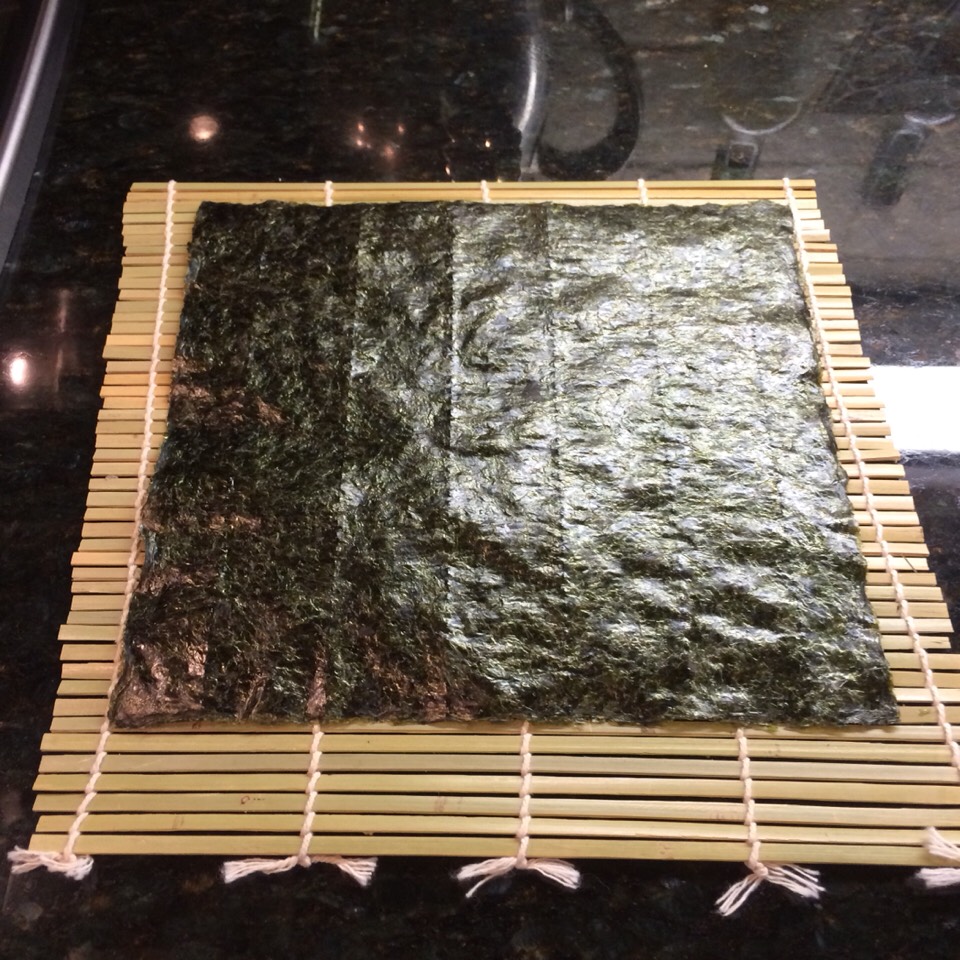 With the veggies ready, place the seaweed paper on the bamboo board. The seaweed paper should face shiny side up, and the bamboo board should face smooth side up.
