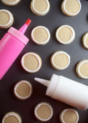 With a squeeze bottle, pipe and outline the cookies in white. Then thin the icing to create a flood consistency. Add a few drops of water at a time to the white icing until it is the consistency of thick syrup. Repeat with the pink icing.