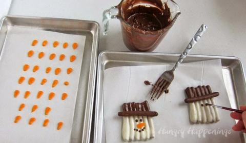 Use a food use only paint brush, to paint chocolate eyes and a mouth onto each snowman.

Attach one orange carrot nose to each snowman using a dab of white chocolate.

Chill for 2-3 minutes until hardened. 