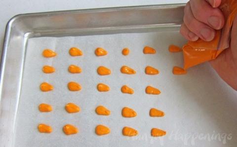 Pour melted orange candy melts into a small zip top bag, and snip off one tip. Pipe small triangle shaped orange carrot noses onto a parchment paper lined baking sheet. Each nose should be about 3/4 inch long. 
Pop tray in freezer for about 2 minutes, until the candy noses are set. 