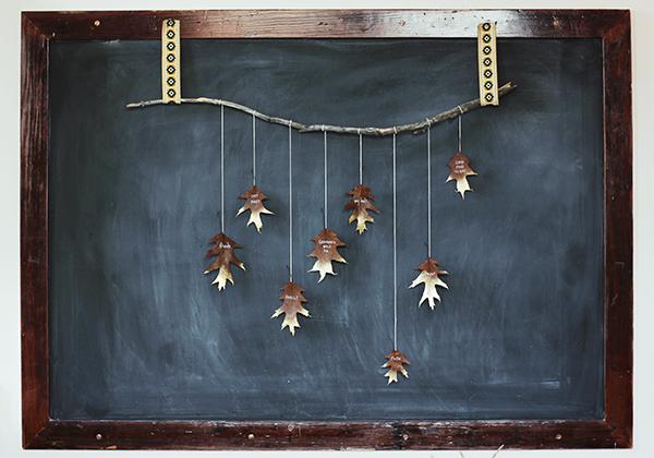 cut two equal lengths of ribbon fold them in half to make loops and nail them to the wall a little closer together than the length of the branch Finally slip the ends of the branch though each of the loops and then attach the leaves to the strings with a little piece of tape or a dab of hot glue.