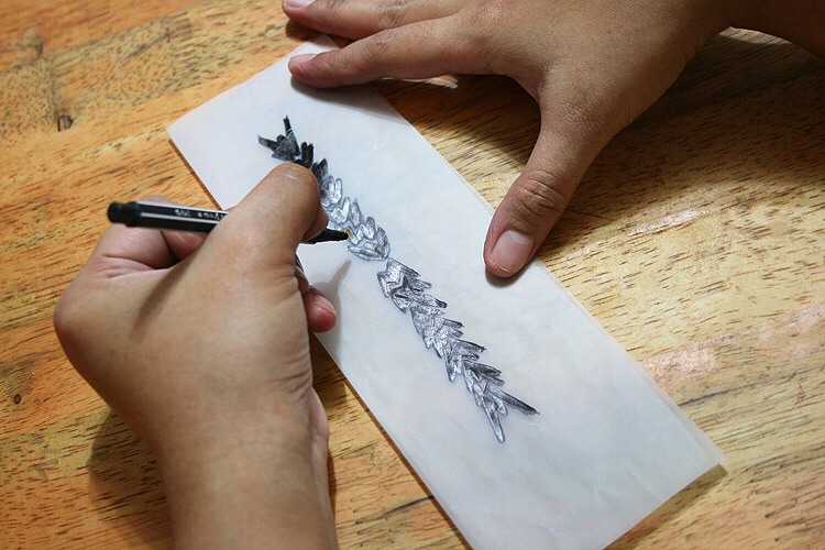 Step 1: Make sure you have a design that you like before using a gel pen in a dark color to draw the design. Simply draw your design on paper such as tracing paper or parchment paper using a pencil, then color in thoroughly using the gel pen.
