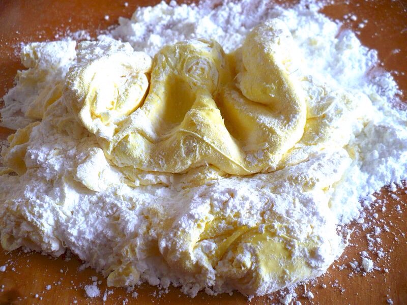 Start folding icing sugar into the marshmallow goo until it becomes a soft and fluffy dough. Grease your hands with a bit of butter and turn the marshmallow out onto a table sprinkled with icing sugar. Continue to knead in icing sugar until the fondant is stiff enough to roll out.