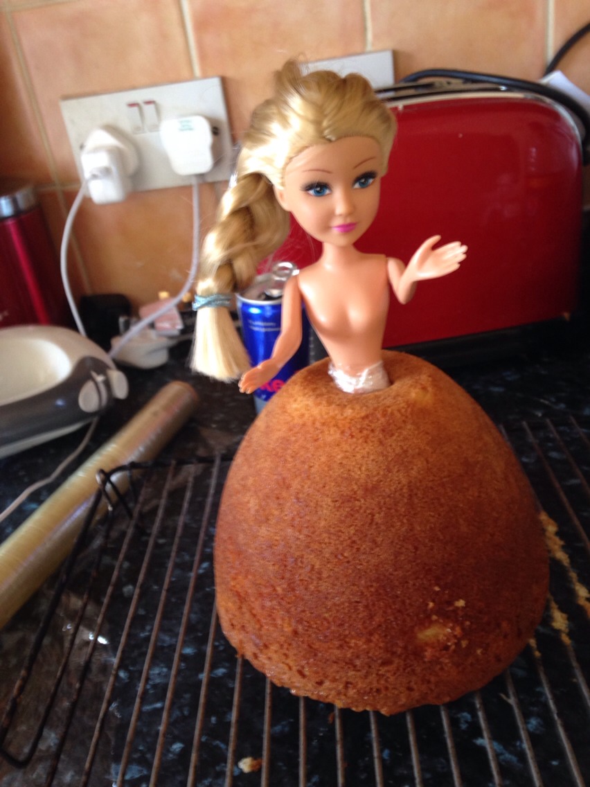 Break legs off blonde barbie like doll and cling film around broken waist ( to prevent plastic shards in cake ) and position in centre of cake