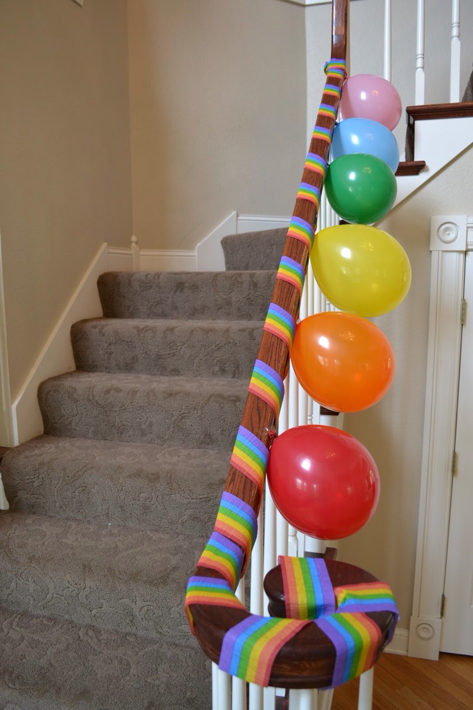 I don't know what that rainbow think is called but tape one side and then go down the stairs and tape at then end and then add balloons.