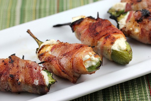 Preheat oven to 400 degrees F (200 degrees C). Line a baking sheet with aluminum foil.
Mix cream cheese and Cheddar cheese together in a bowl until evenly blended. Fill each jalapeno half with the cheese mixture. Put halves back together and wrap each stuffed pepper with a slice of bacon. Arrange ba