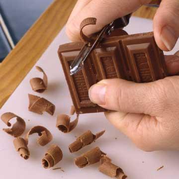 Place a bar or block of chocolate on waxed paper. Make chocolate curls by pulling a vegetable peeler toward you across the flat-test side of the chocolate, pressing firmly in long, thin strokes. Small curls can be made by using the side of the chocolate bar. 