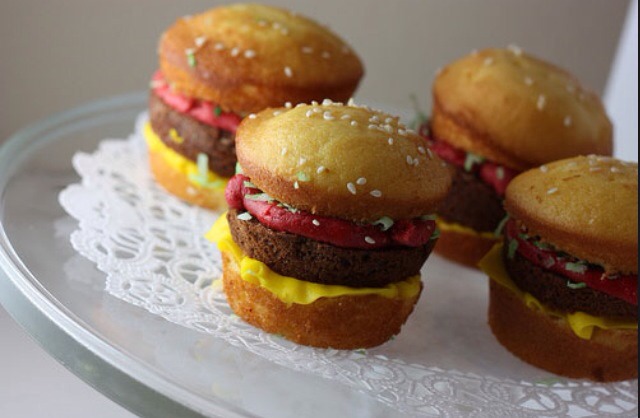 Cut a vanilla cupcake in half for the buns. Put small white tear drop shaped globs of frosting for the sesame seeds. Use read and yellow frosting for ketchup and mustard. Use brownie or chocolate cake for the patty. 