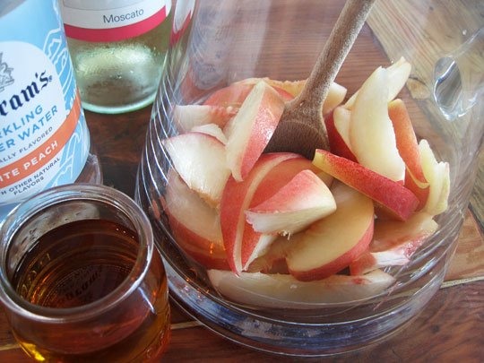 How to:
- In a pitcher place 3/4 of the sliced peaches (saving some for garnish) and brandy and lightly muddle.
- Then Add the Moscato and seltzer water.
- Stir with wooden spoon to mix. 
- Pour into ice filled glasses and top with a couple of fresh peach slices.