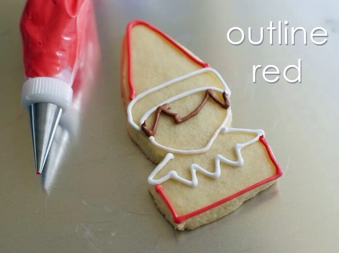 Use a #2 tip to outline the hat and shirt in red. 

Thin the all of the icings with water, a bit at a time, until it is the consistency of thick syrup.  Cover with a damp dish towel and let sit several minutes.

Stir gently with a rubber spatula and transfer icings to squeeze bottles.
