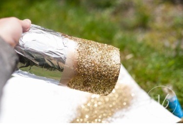 Take your spray paint and give quick sweeping motions to cover the piece, immediately sprinkle glitter over the wet spray paint, making sure you cover as much of the paint as possible. Use a piece of paper to catch extra glitter so you can put it back in the container to use again later!