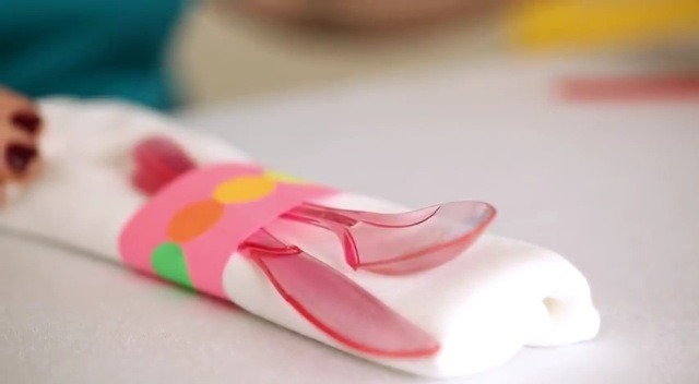 Cut a strip of baby (2 by 12) or just a enough paper to go around your folded napkin then decorate with stickers and tape onto your folded napkin.