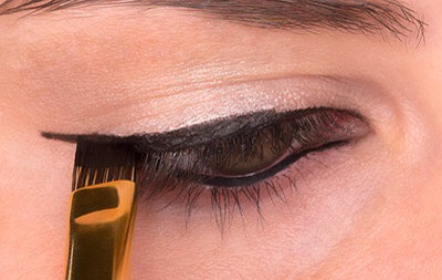 STEP 1
Dip your brush in eyeliner and gently drag it along the lash line and past the top outer corner of your eye. You want the brush to follow the upward curve of your eye. For a more dramatic winged look, draw farther out and angle the liner slightly more.