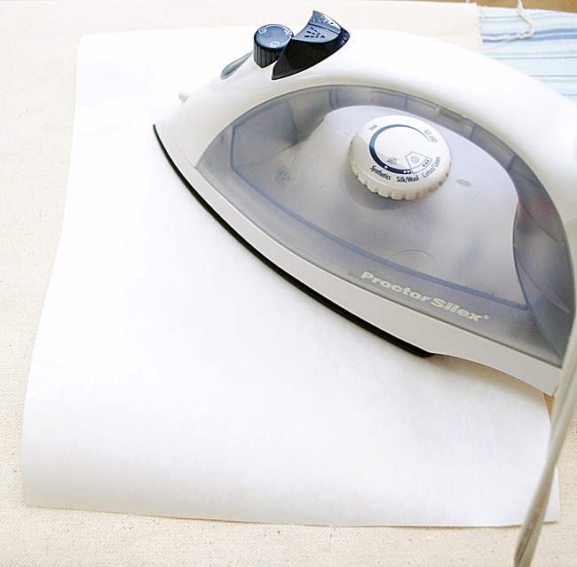 Step 1: Start with a freshly ironed piece of fabric. 
Cut out a section of freezer paper, approximately 8 1/2″ by 11″, and iron it (shiny side facing towards the fabric) to the fabric until it adheres nicely.