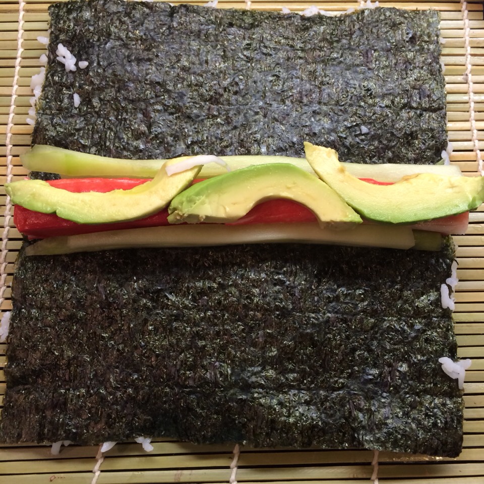 Gently flip the paper over. Once upside down place the crab, cucumber, and avocado on the paper. If the crab meat was not pre cooked/sliced, steam accordingly and slice ( but not too thin ).