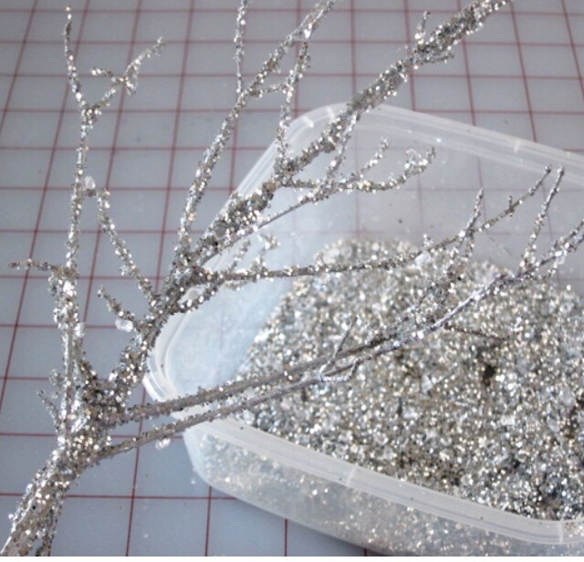 I am showing this step on a small branch, container, and table, but if you have large branches – lay a cookie sheet on the ground and sprinkle the glitter onto your branch so the excess glitter falls onto the cookie sheet and you can re-use it. Do this outside so glitter won't get all over the place