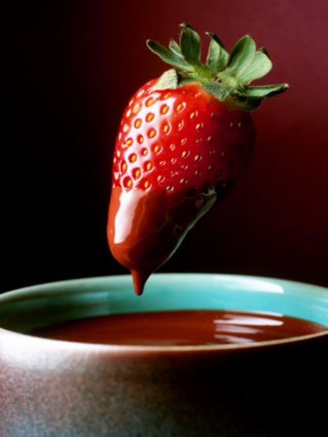 Step 3
Once the chocolates are melted and smooth, remove from the heat. Line a sheet pan with parchment or waxed paper. Hold the strawberry by the stem, dip the fruit into the dark chocolate, lift and twist slightly, letting any excess chocolate fall back into the bowl. Set strawberries on the pan