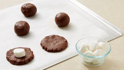 3) Shape dough into 12 (2-inch) balls. Flatten each ball into 3-inch round. Shape 1 cookie dough round around 1 marshmallow half, covering completely. Repeat with remaining dough rounds and marshmallows. Place 2 inches apart on cookie sheets.
