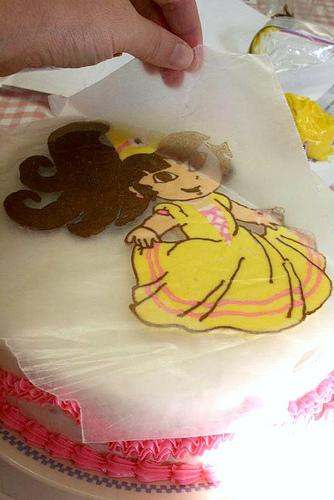 Take your coloring design out of the freezer and make sure the icing is nice and hard. 

Un-tape the wax paper/icing, and quickly but carefully, up-end your design onto the cake. Press it down a little so it sticks. 

Then, also quickly but carefully peel back the wax paper to reveal the design.